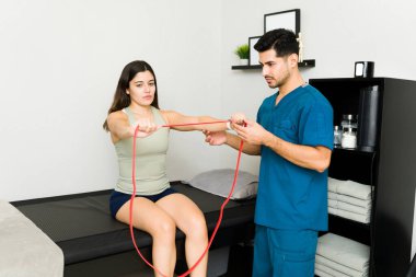 Fiziksel rehabilitasyon egzersizlerimi yapıyorum. Güzel genç bir kadın fizik tedavi sırasında direnç bandı çekiyor.