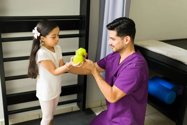 男性理疗师帮助儿童患者进行理疗 西班牙男人在诊所给一个女孩一个哑铃重量 — 图库照片