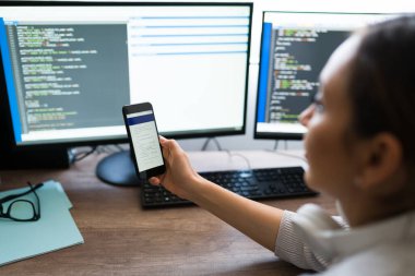 Profesyonel genç kadın ve programcı akıllı telefonunda kod yazılım uygulaması üzerinde çalışıyor mu diye kontrol ediyor.