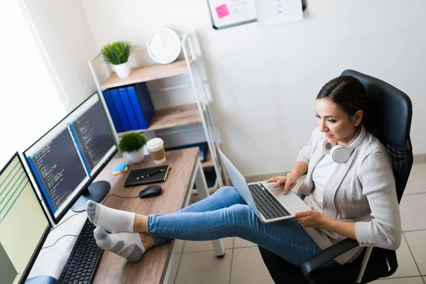 自宅からソフトウェアアプリをコーディング中に彼女のオフィスの机の上に彼女の足を休ませて裸足の若い女性のトップビュー — ストック写真