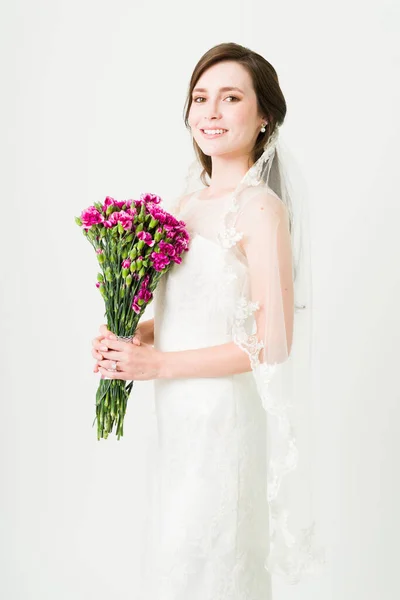 美しいウェディングドレスと白いスタジオの背景の前のベールに身を包んだ豪華な若い花嫁 — ストック写真