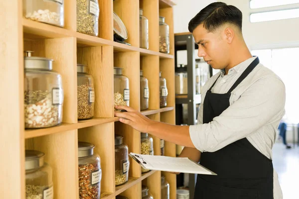 Checking the organic products. Male employee doing an inventory while looking at the shelves and containers with nuts and dry food