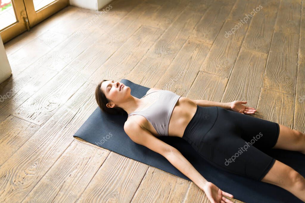 Relaxing with a savasana pose. Fit young woman practicing breathing exercises while doing a corpse yoga pose