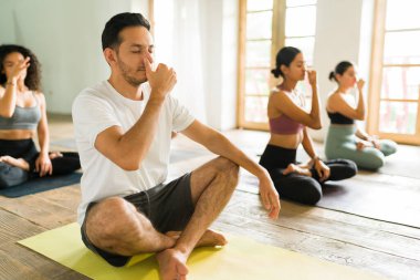 30 'lu yaşlarında yakışıklı bir adam nefes egzersizleri yaparken ve yoga dersinde meditasyon yaparken gözleri kapalı rahatlıyor.