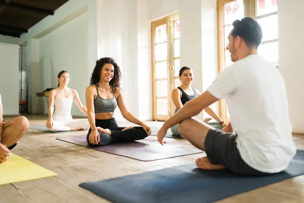 Hispanic male yoga instructor talking about pranayama breathing exercises with his students before starting a group class