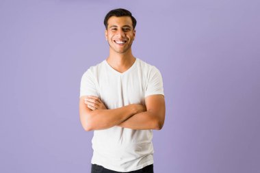 Yakışıklı Latin genç adam gülümsüyor ve parlak mor bir arka planda kameraya bakıyor.