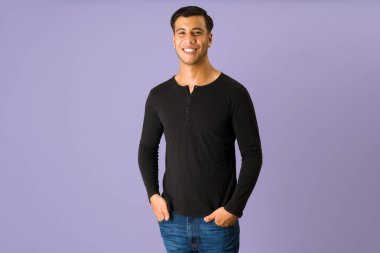 Yakışıklı, sıradan kıyafetler giyen ve elleri cebinde kameraya bakan adam.