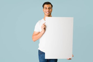 Yakışıklı İspanyol adam kameraya bakıyor ve büyük bir teklif sunarken elinde boş bir ilan taşıyor. 