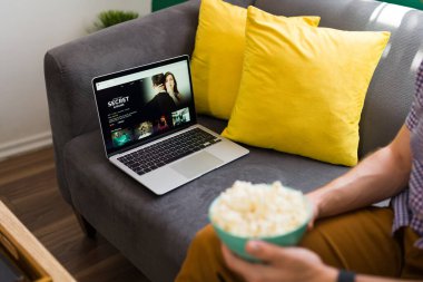 Filmin tadını çıkarıyorum. Genç adam dizüstü bilgisayarında televizyon dizisi izlerken kanepede dinleniyor.