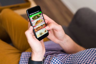 Ben acıktım. Akıllı telefonuyla yemek dağıtım uygulamasına bakan ve internetten yemek sipariş eden bir adamın elleri.