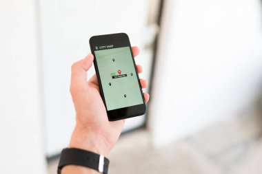 Erkek, akıllı telefonu tutuyor ve navigasyon haritası uygulamasında şehir adresini arıyor. 