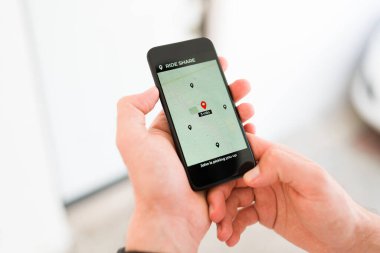 Sürücüyü beklerken elinde akıllı telefon tutan ve gezinti paylaşım uygulamasındaki navigasyon haritasına bakan kişi 