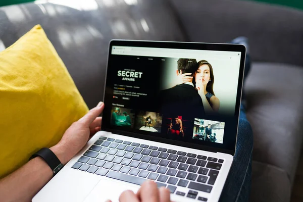 Yayın servisi. Kanepede dinlenirken internetten izlemek için film ya da dizi arayan yetişkin biri.