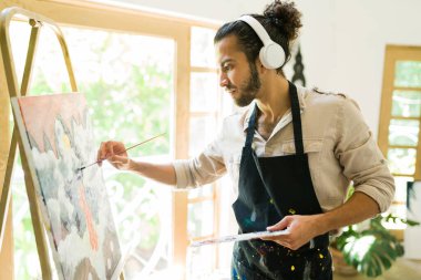 Sanat aktiviteleriyle rahatlamak. Genç adam bir sanat eseri çizerken kulaklıkla müzik dinliyor.