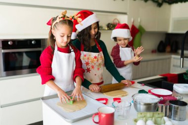Güzel, genç bir anne merdaneyle güzel çocuklarıyla kurabiye hamuru yapıyor. 