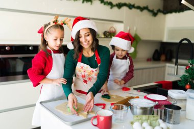 Neşeli aile kurabiyeleri fırına koymak üzere. Annem ve çocukları Noel tatlısı pişiriyor.