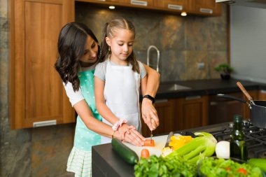 Annemle yemek pişiren küçük kız yardımcı. Sevgili anne kızıyla sebze doğruyor.