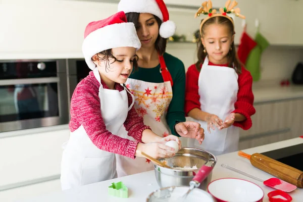 Noel Baba şapkası takan küçük şirin bir çocuk kurabiye hamuruna annesi ve kız kardeşiyle yumurta karıştırıyor.