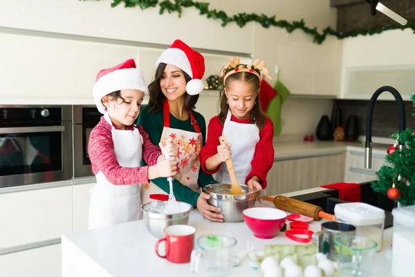 デザートのお母さんを助ける 愛らしい娘と息子の混合バッターとアイシングにクリスマスクッキーを焼く — ストック写真