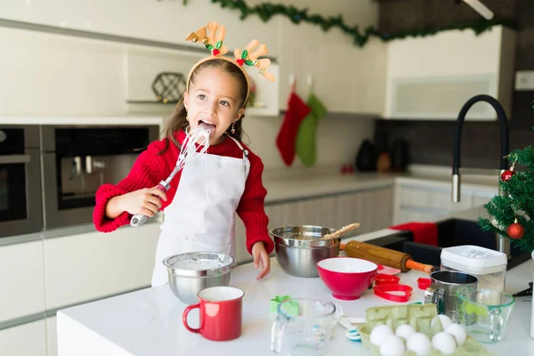 糖分很高漂亮的小女生一边吃糖霜 一边在厨房里搅拌配料烘焙 — 图库照片