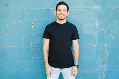 30 'lu yaşlarındaki çekici Latin adam siyah tişört giyerken gülümsüyor ve özel yapım baskısını gösteriyor.