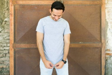 30 'lu yaşlarda yakışıklı bir adam dışarıda dikiliyor ve üzerinde parmak izi tasarımı olan gri bir tişört giyiyor.