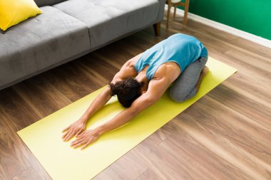 Genç bir adamın vücudunu bir çocuğun duruşuyla germesinin yüksek açısı. Formda adam evde yoga yapmayı bitiriyor.