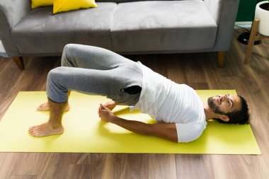 Çekirdek kuvveti. Genç adam gülümsüyor ve evde egzersiz yapıyor. Latin adam briç pozisyonunda yoga yapıyor.  