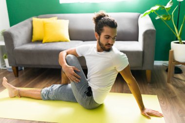 Odaklanmış genç bir adamın portresi. Balıkların efendisi pozu veriyor ve evde yoga egzersizi yapıyor.