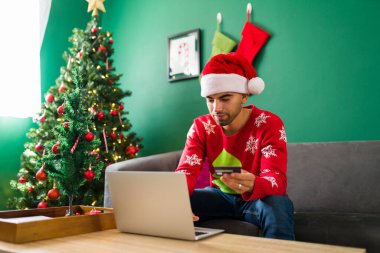 Son dakika alışverişi. Çekici genç adam internetten noel hediyesi alıyor ve kredi kartıyla ödüyor.