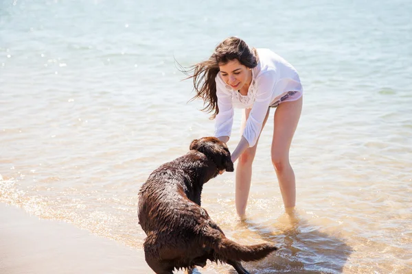 Brunett försöker få sin hund i vattnet — Stockfoto