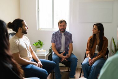 Akıl sağlığı destek grubuna katılan insanlar, bir adamın konuşmalarını dinleyip deneyimlerini paylaşıyorlar.