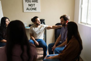 Destek grubu oturumunda bir çemberde oturan bireyler, başka bir katılımcıya rahatlık sunan bir adam