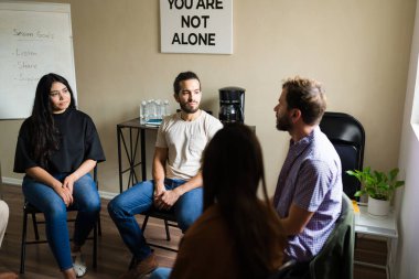 Bir çemberin içinde oturan umut dolu insanlar, ruh sağlığı toplantısı sırasında hislerini paylaşıyorlar ve rahatlıyorlar. Yalnız değilsin.