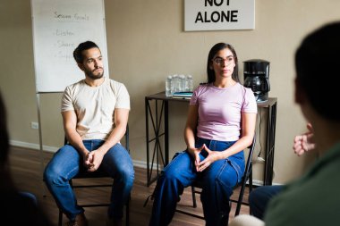 Hispanik yetişkinler bir bağımlılık destek grubu oturumuna katılıyor, dikkatle dinliyor ve paylaşılan deneyimlere odaklanıyor