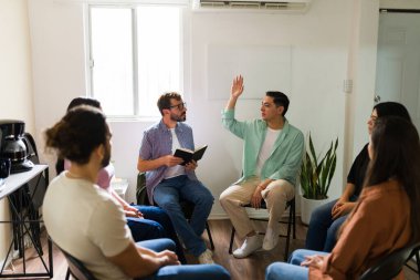Çemberde oturan bireyler, bir terapistin önderliğindeki zihinsel sağlık tartışması sırasında paylaşmak için elini kaldıran bir adam.