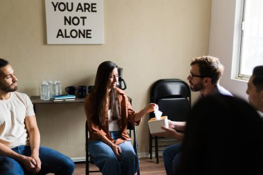 Bir kadın grup terapisi ya da destek grubu toplantısı sırasında bir erkekten mendil alırken üzgün ve ağlıyor