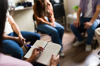 Bir grup insan bir çemberde bir araya gelip notlar alırken akıl sağlığı, bağımlılık ya da keder için danışmanlık ve destek alıyorlar.