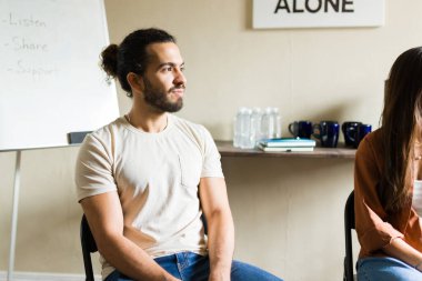 Bir destek grubu toplantısında aktif olarak dinleyen bir adam güvenli bir ortamda zihinsel sağlık desteği ve bağımlılık tedavisi arıyor.