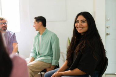 Çeşitli insanlar bir destek grubu toplantısına katılıyor, kameraya gülümseyen genç bir kadın, umudu ve toplumu buluyor.