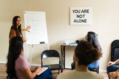 Grup terapisi seansına başkanlık eden kadın terapist, destekleyici bir zihinsel sağlık ortamının katılımcılarına oturum hedeflerini açıklıyor.