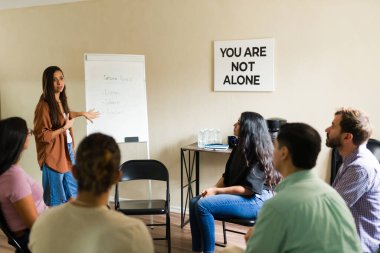 Çeşitli bir destek grubuna başkanlık eden terapist, ruh sağlığı ve bağımlılık tedavisi için oturum hedeflerini tartışıyor