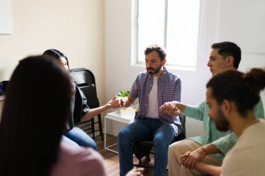 Bir grup insan el ele tutuşarak bir çemberde oturuyor, bir destek grubunda duygusal bağ ve topluluk buluyor.