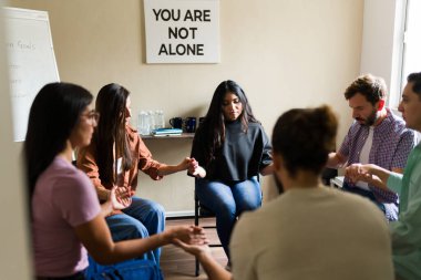 Bir grup insan bir çemberde oturuyor, el ele tutuşuyorlar ve terapi sırasında duygusal destek alıyorlar.