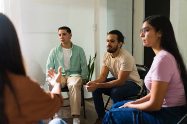Çemberde oturan çok ırklı yetişkinler, grup terapisi sırasında dinleyip konuşarak zihinsel sağlığa destek sağlıyorlar.