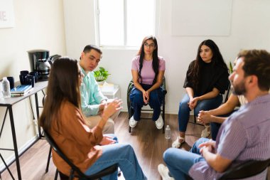 Çeşitli insanlar bir çemberde oturup grup terapisi sırasında dinleyip konuşuyorlar. Duygusal destek ve danışmanlık sağlıyorlar.