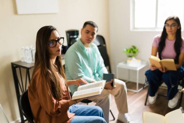 Bir kitap kulübü toplantısı sırasında elinde kitap tutan, aktif olarak katılan ve görüşlerini paylaşan bir grup genç yetişkin.