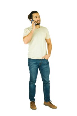 Saçları topuz ve sakallı genç adam beyaz arka planda duruyor, akıllı telefonla konuşurken gülümsüyor, gündelik modern yaşam tarzı sohbet ediyor.