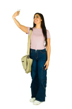 Stüdyoda uzun uzun gülümseyen genç bir kadın, elinde akıllı bir telefonla temiz beyaz bir arkaplanda sıradan bir selfie çekiyor.