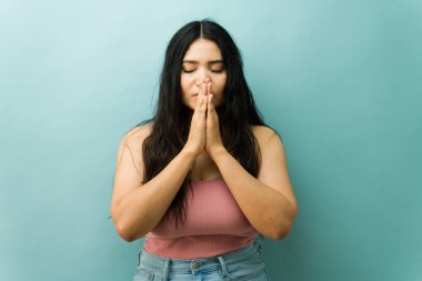 İspanyol kadın gözleri kapalı ve elleri sımsıkı sarılmış olarak duruyor. Dua ederek meditasyon yapıyor, huzur, inanç ve iç huzuru yayıyor.